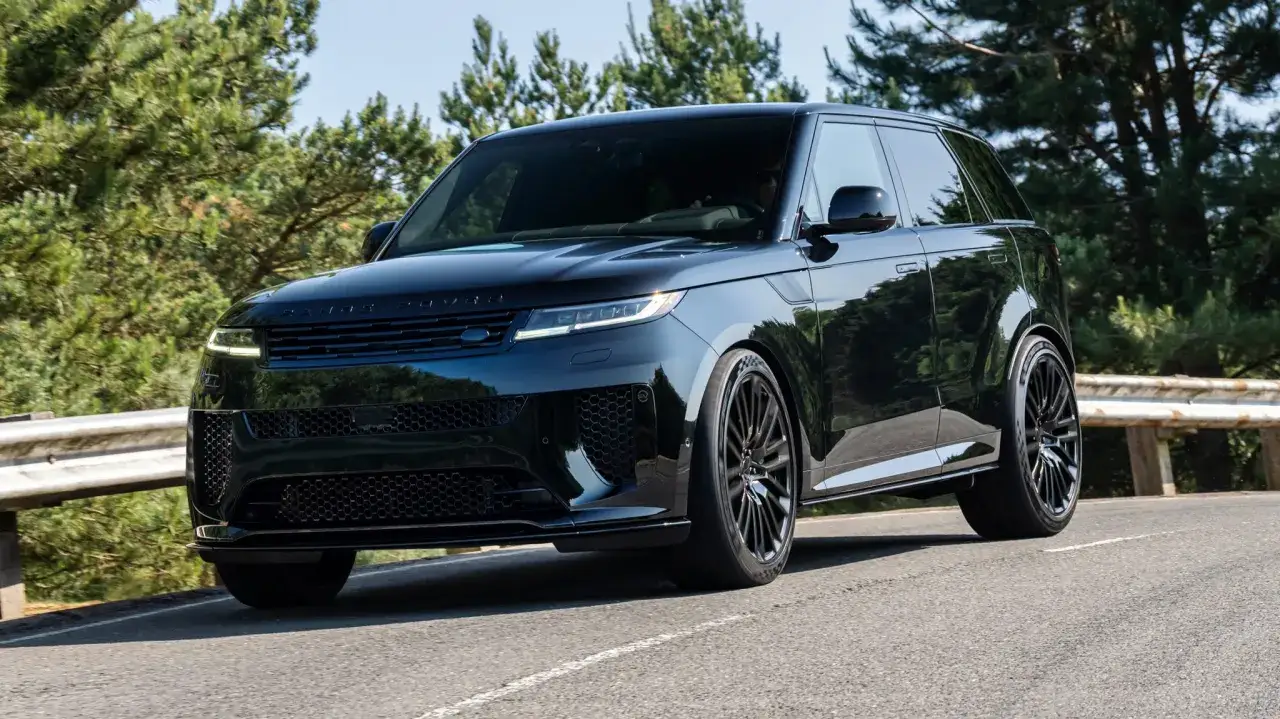 Schwarzer, teuerster Range Rover gleitet auf einer asphaltierten Straße durch eine grüne Landschaft.