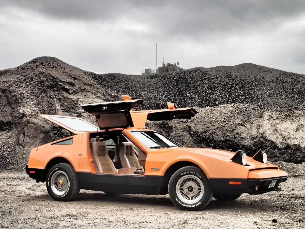 Orange Bricklin SV1 mit Flügeltüren steht auf Schotter vor einer Kiesgrube.