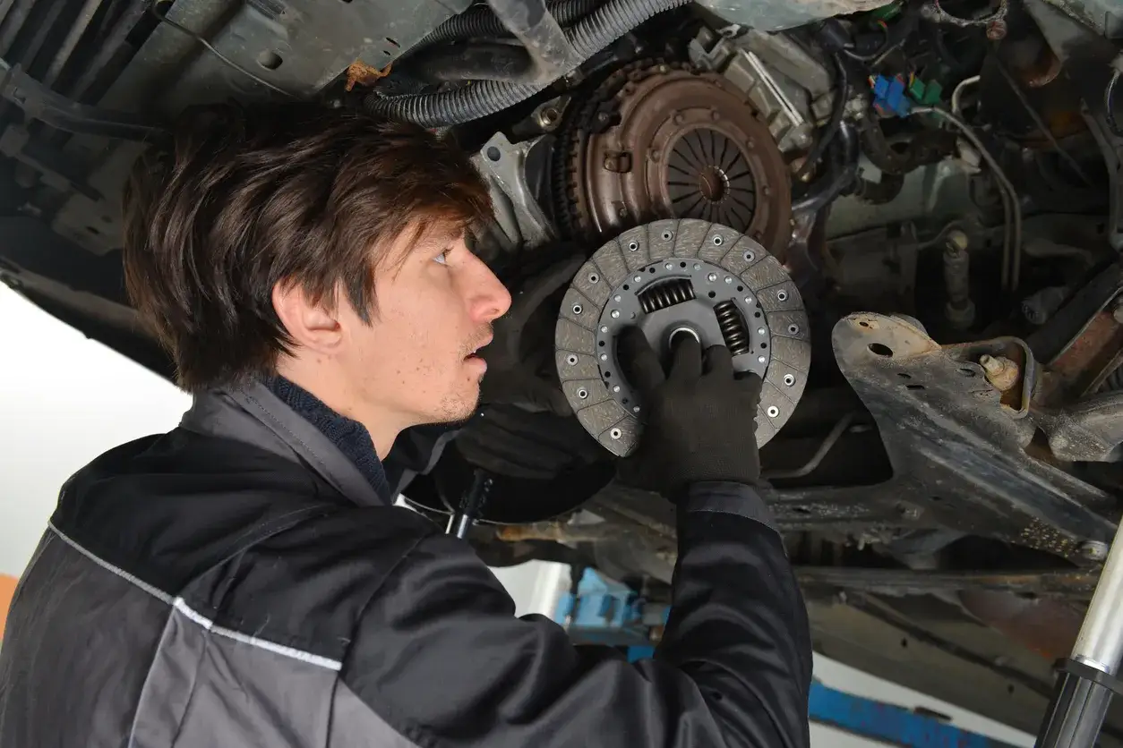 Mechaniker hält neue auto kupplung in der Hand, bereit für den Einbau unter dem Auto.
