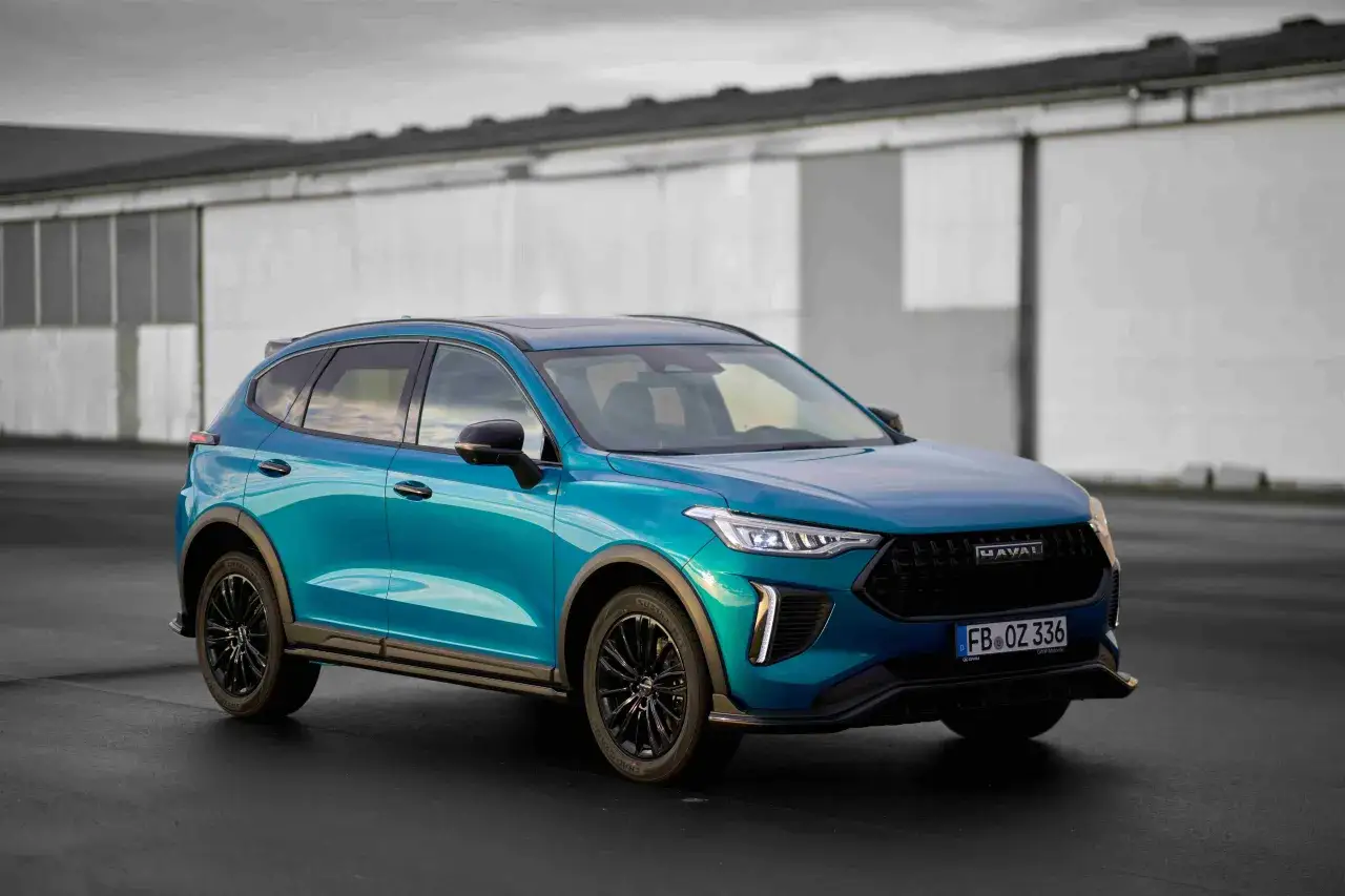 Türkisfarbener Haval SUV von Great Wall Motor steht auf Asphalt vor einem Gebäude.