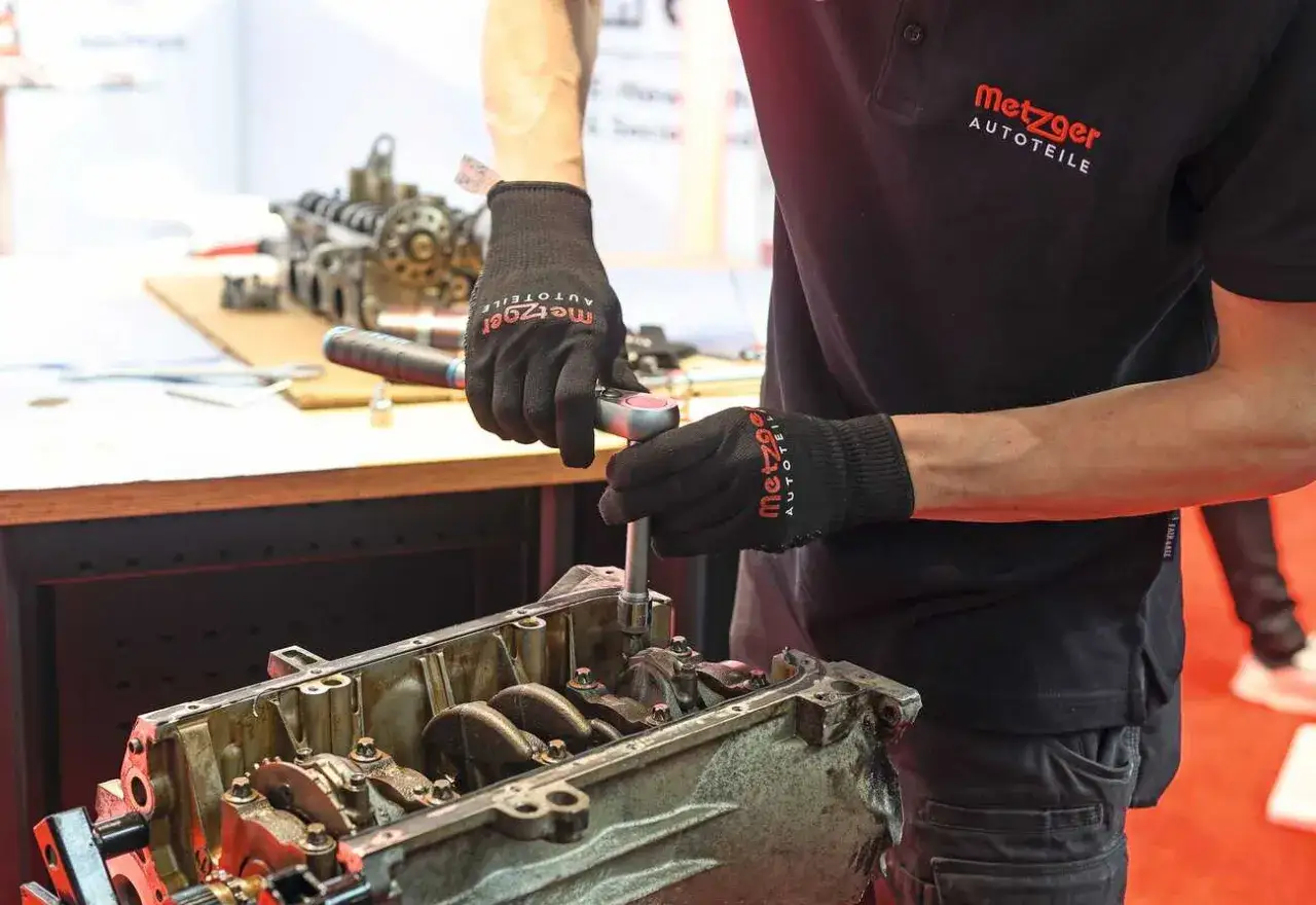 Mechaniker mit Metzger Autoteile Handschuhen repariert einen Motor. Die Erfahrung mit Metzger Autoteile zahlt sich aus.