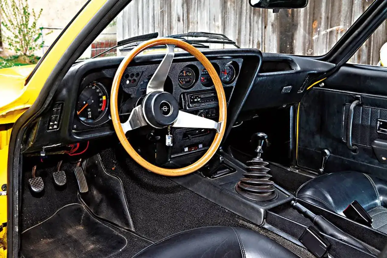 Der opel gt innenraum zeigt ein Holzlenkrad, klassische Instrumente und einen Schaltknüppel.