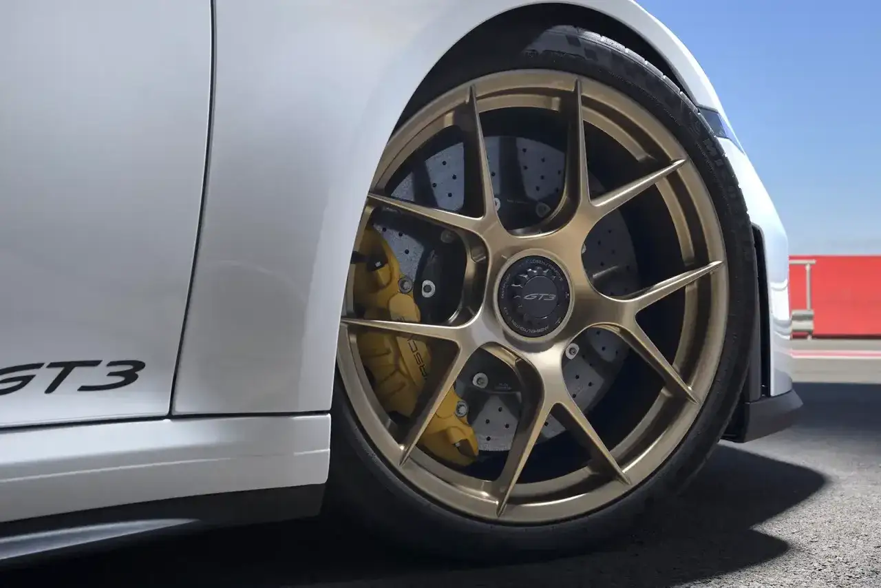 Detailaufnahme eines Porsche GT3 mit goldenen Felgen und gelben Keramik Bremsen. Die Keramik Bremsen Kosten sind hoch, aber die Performance ist unschlagbar.