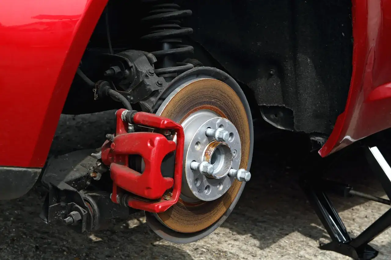 Rotes Auto mit ausgebautem Rad, um die Bremse zu inspizieren. Ein Wagenheber stützt das Fahrzeug.