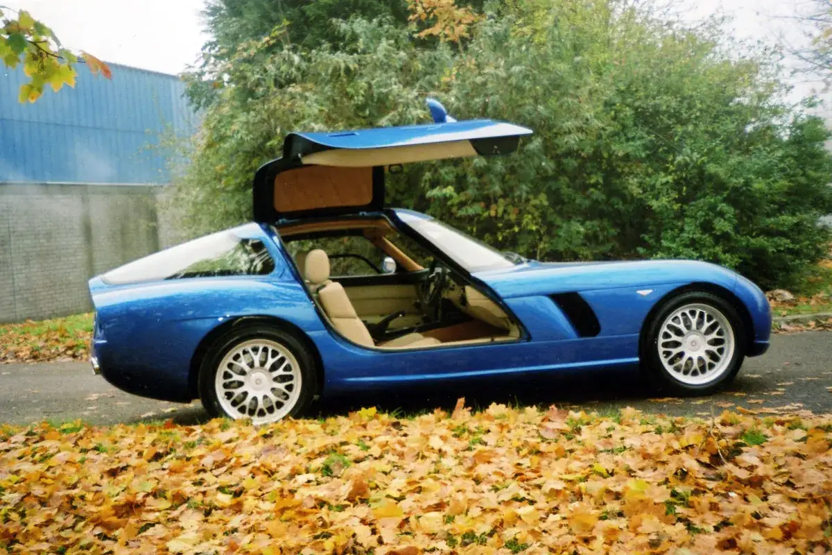 Blauer Bristol Fighter mit Flügeltüren, bereit für eine Spritztour im Herbstlaub.
