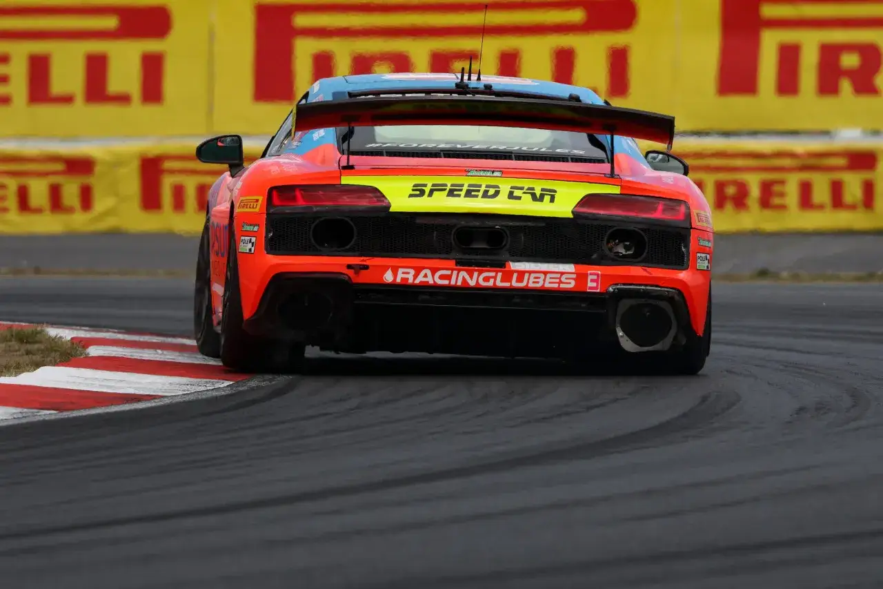 Ein leuchtend oranger Audi R8 GT4 rast über die Rennstrecke, mit Pirelli-Werbung im Hintergrund.