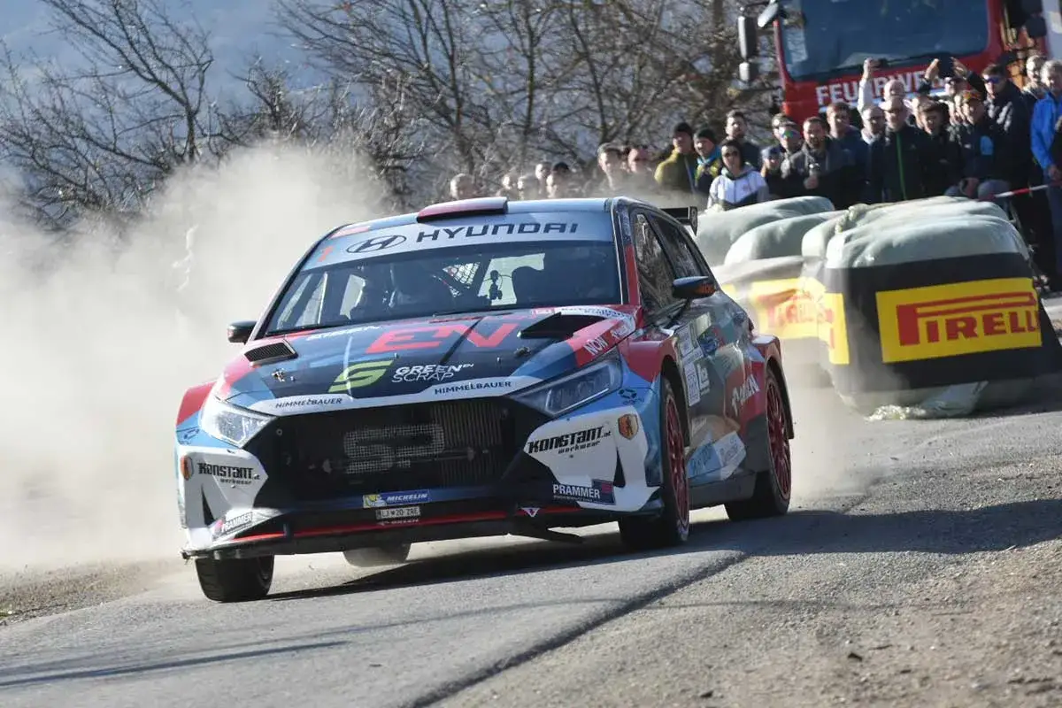 Ein Rallyeauto der Rebenland Rallye rast durch Staub, Zuschauer jubeln.