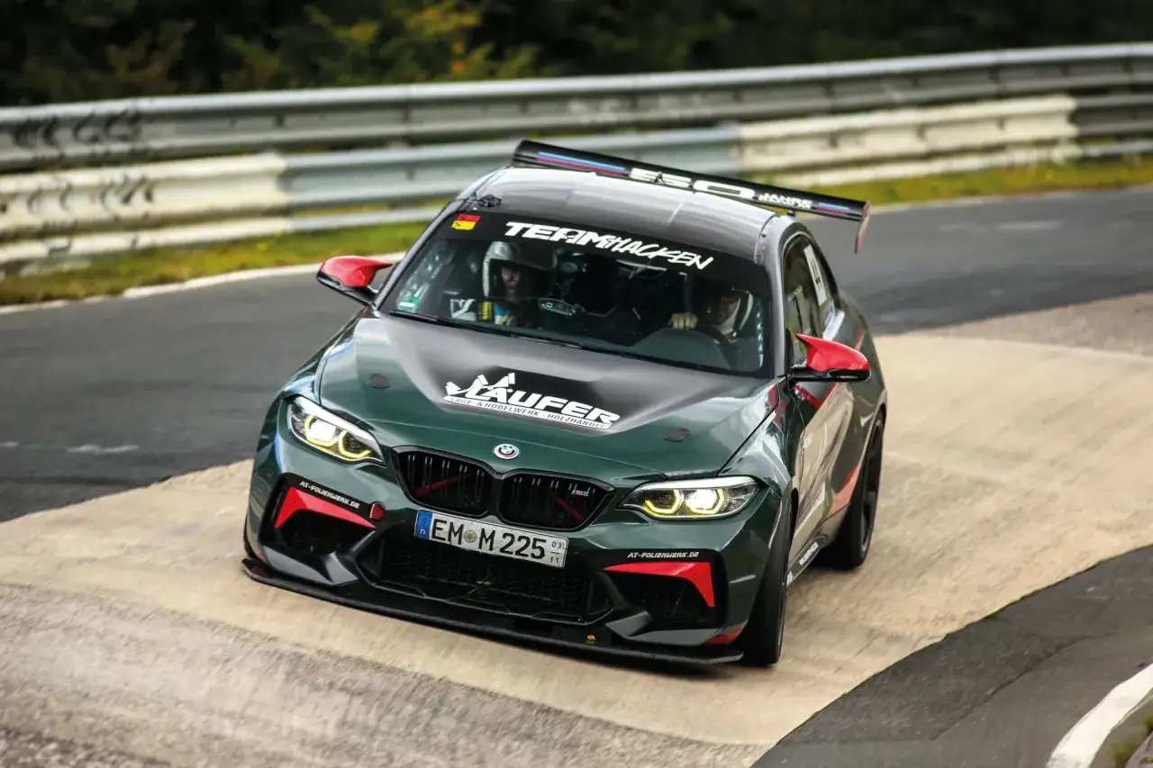Grüner BMW M2 Competition mit roten Spiegelkappen auf Rennstrecke.