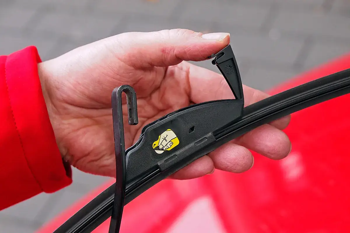 Hand wechselt Scheibenwischer vorne am Toyota Yaris. Der Wischerarm wird mit dem Haken eingehängt.