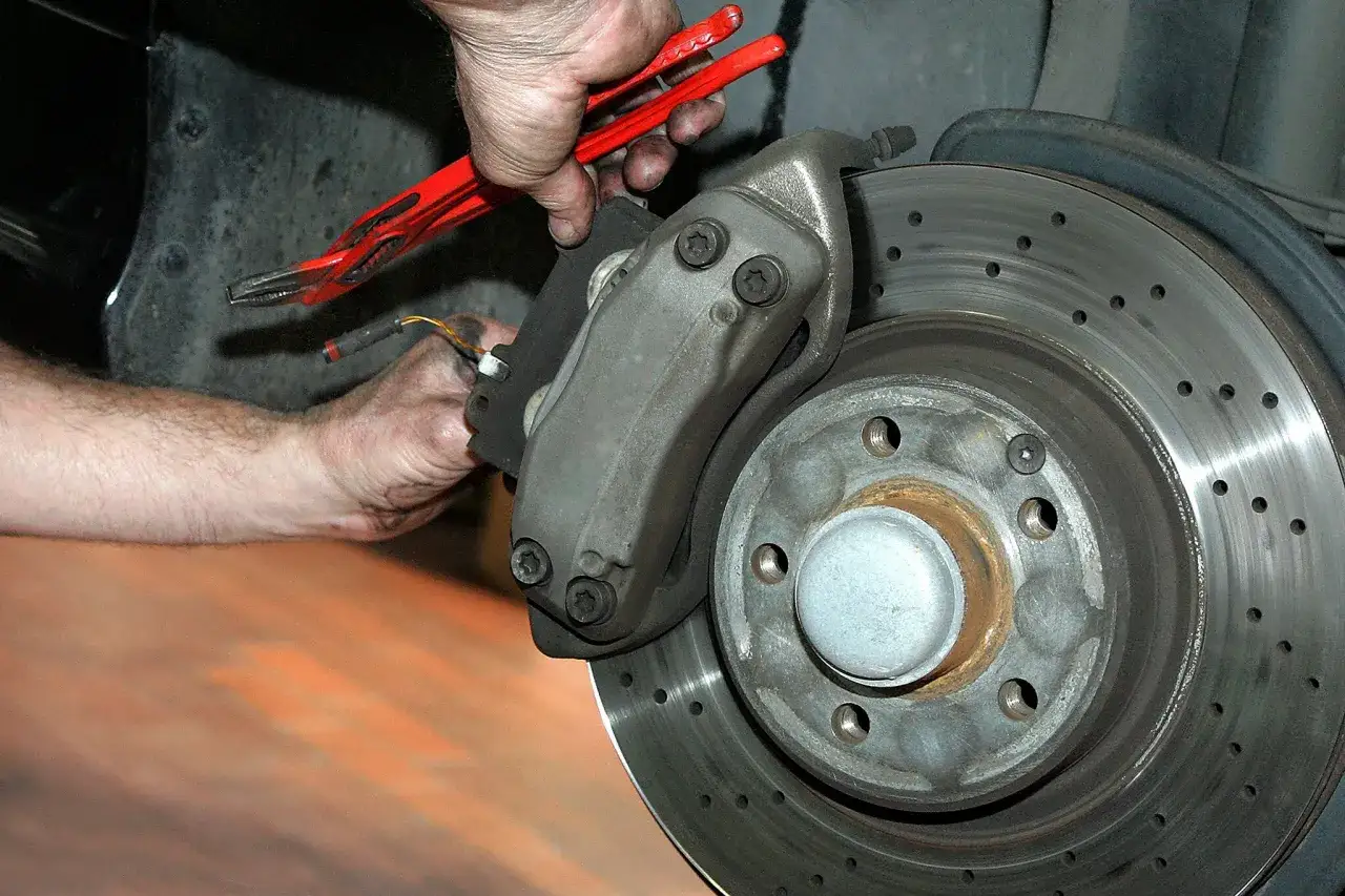 Mechaniker repariert Bremsen, ob Brembo oder ATE, mit Werkzeug am gelochten Bremsscheiben.
