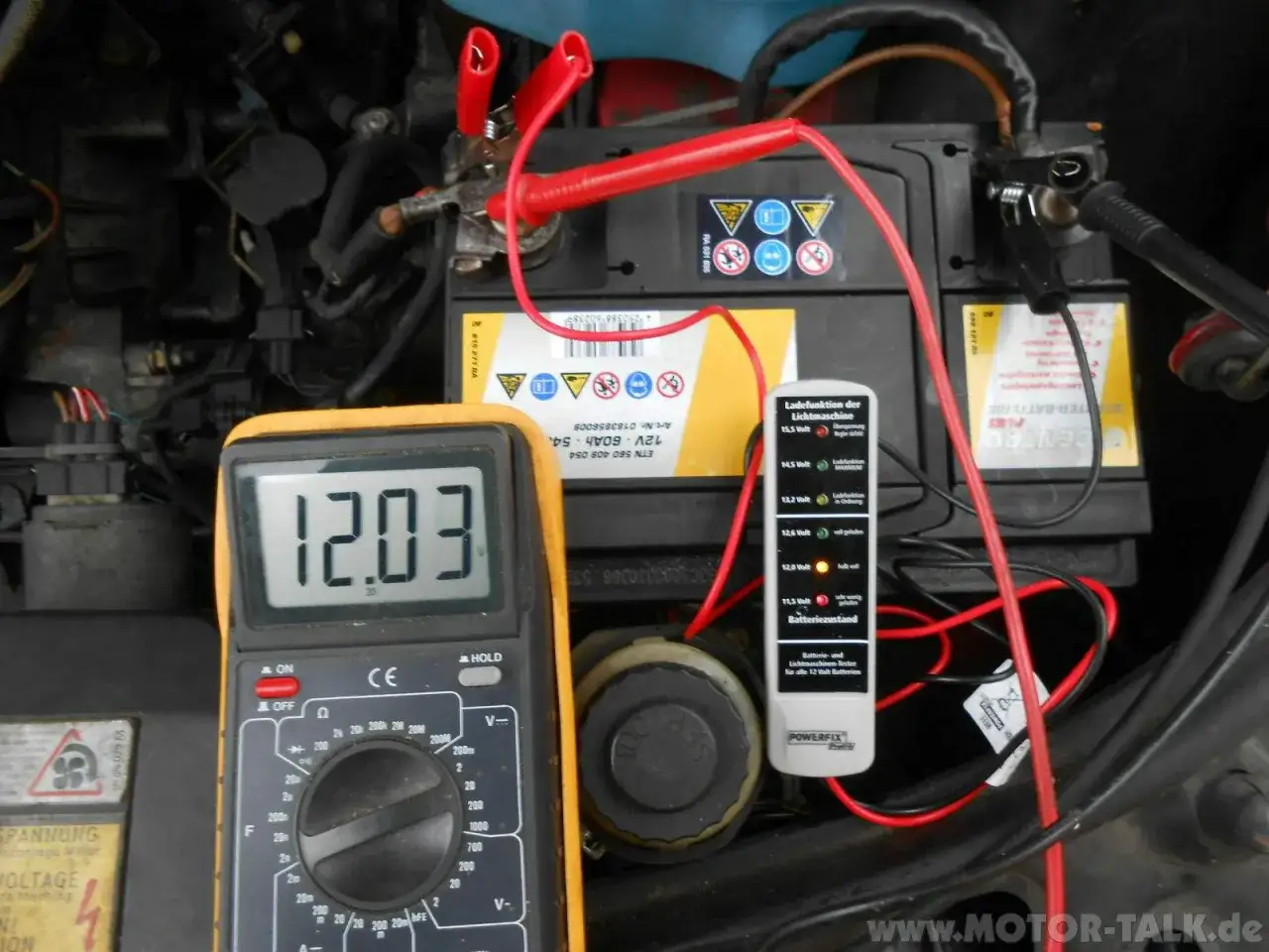 VW p0562: Multimeter zeigt 12,03 Volt an einer Autobatterie an. Ein Lichtmaschinen-Tester liegt daneben.