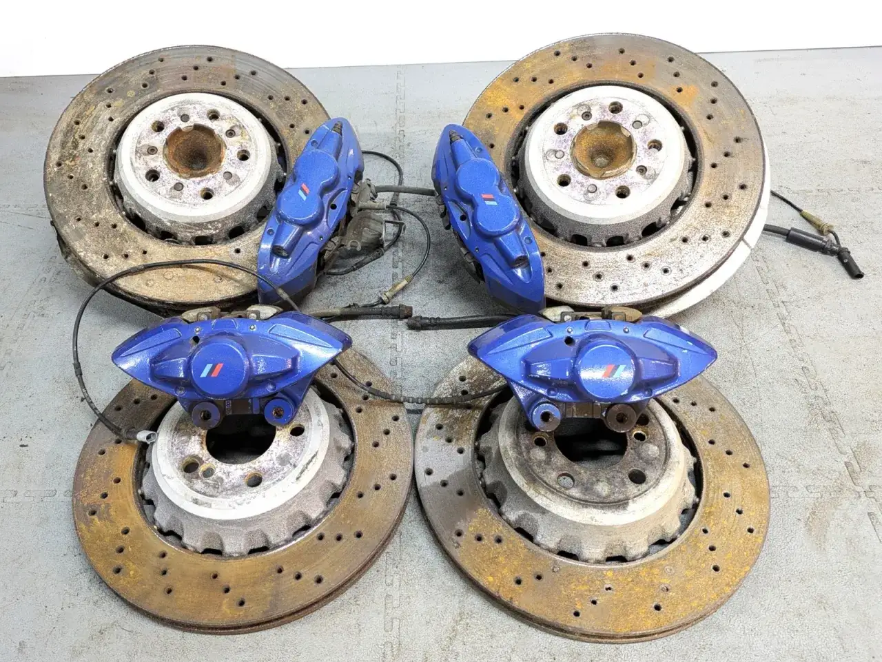 Vier BMW M4 F82 Bremsscheiben mit blauen Bremssätteln und dem M-Logo.