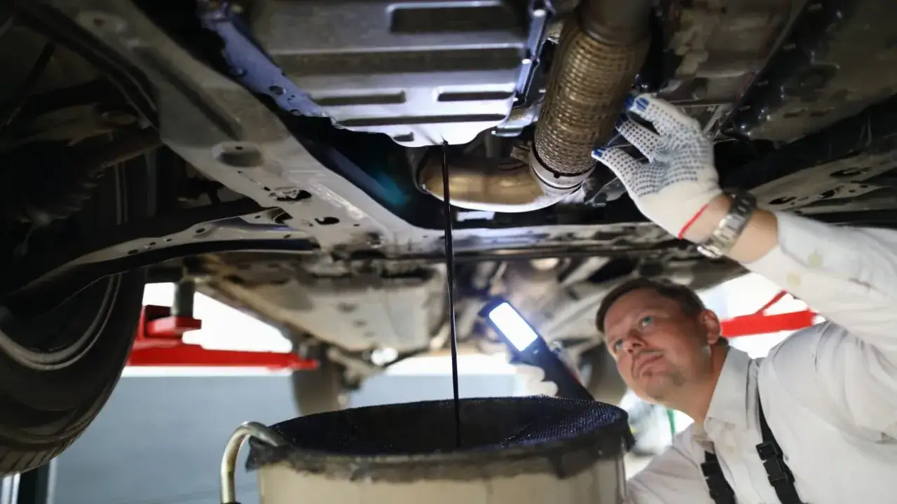 Mechaniker entsorgt Altöl aus einem Auto. Der Mann mit Handschuhen und Lampe prüft den Ölwechsel.