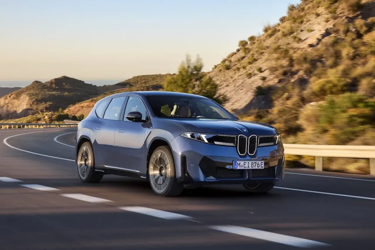 Blauer BMW iX3 fährt auf kurviger Straße. Informieren Sie sich über die aktuellen Lieferzeiten für Ihren BMW iX3.