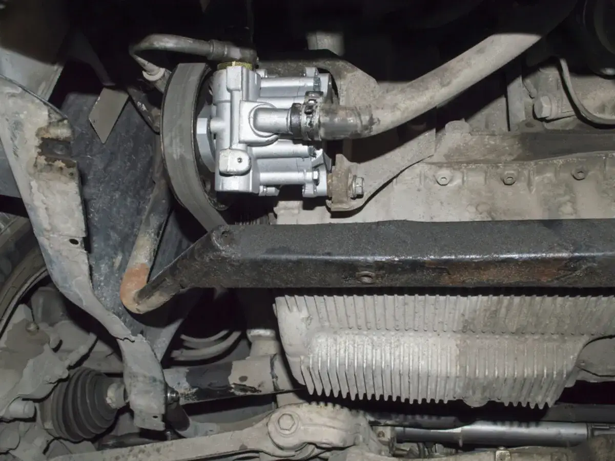 Unterseite eines Autos mit sichtbarer Servopumpe und Keilriemen. Möglicherweise ist die Servolenkung ausgefallen.
