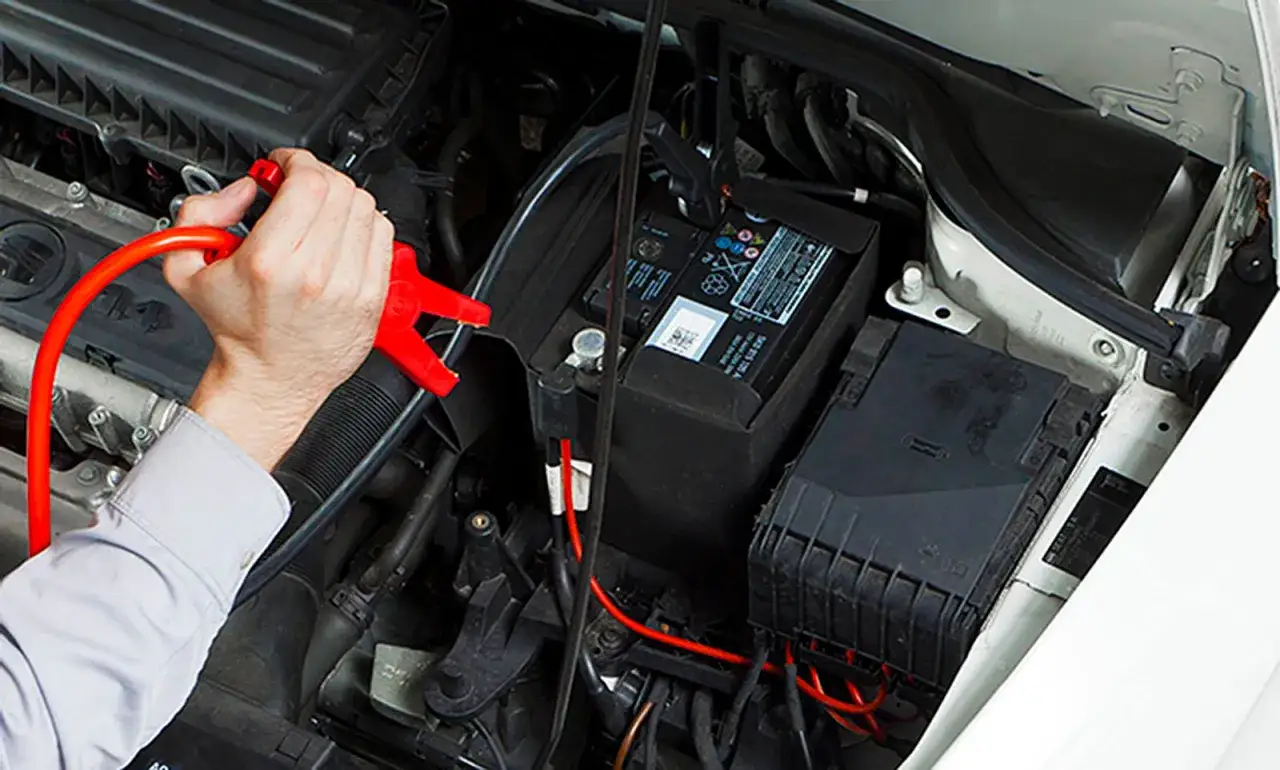 Hand klemmt Starthilfekabel an Autobatterie im eingebauten Zustand.