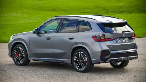 Grauer BMW X1 23d steht auf Asphalt vor grüner Wiese.