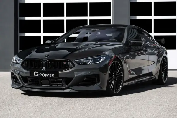 Ein getunter BMW M850 Gran Coupé in dunklem Grau mit Carbon-Elementen und auffälligem Heckspoiler steht vor einer Garage.